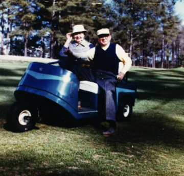 Osborn and wife sitting on a blue golf cart on the greens